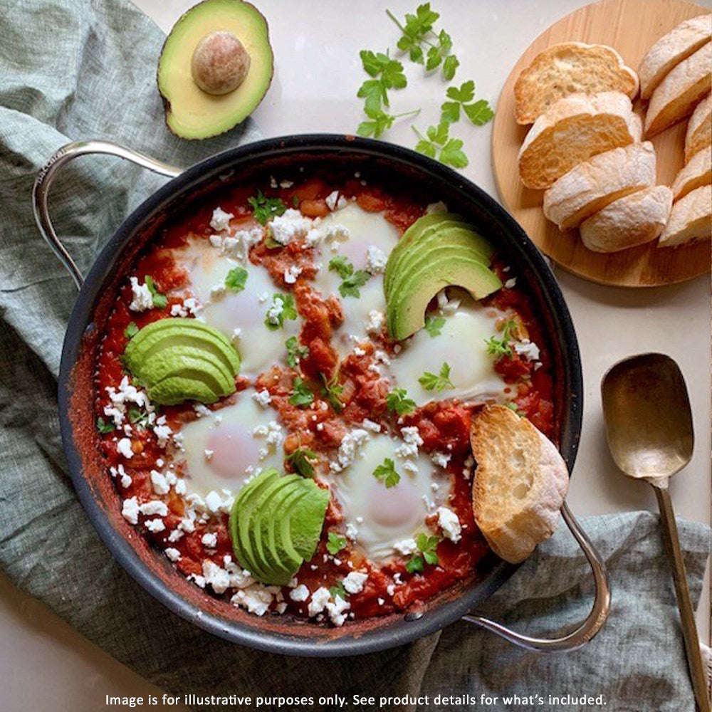 A serving of shakshuka topped with avocado slices feta cheese and herbs - Baccarat id3 non stick pan