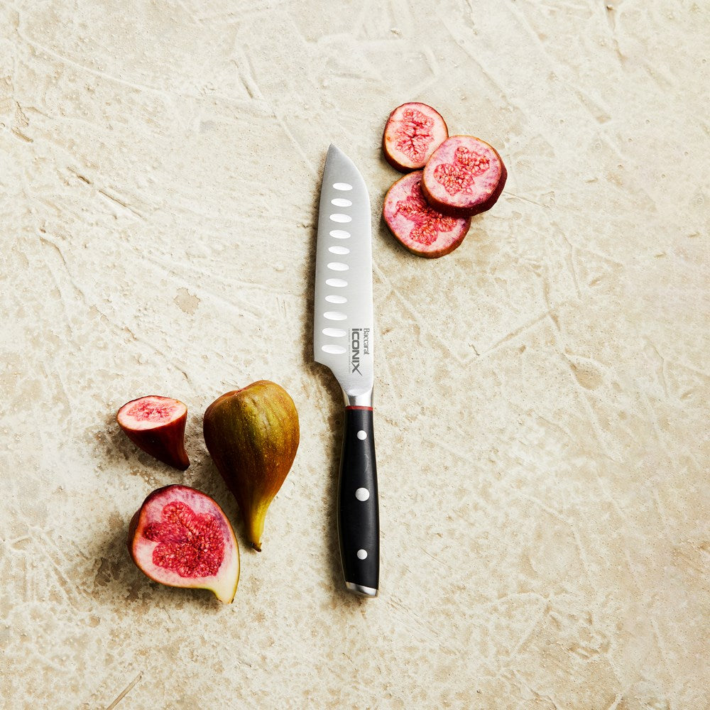 A sleek utility knife with a black handle beside sliced figs on a light surface - Baccarat Iconix