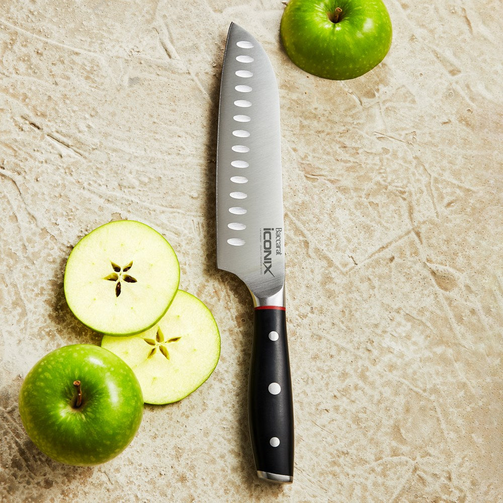 A sleek Baccarat Iconix Santoku Knife with a black handle and silver blade beside its packaging