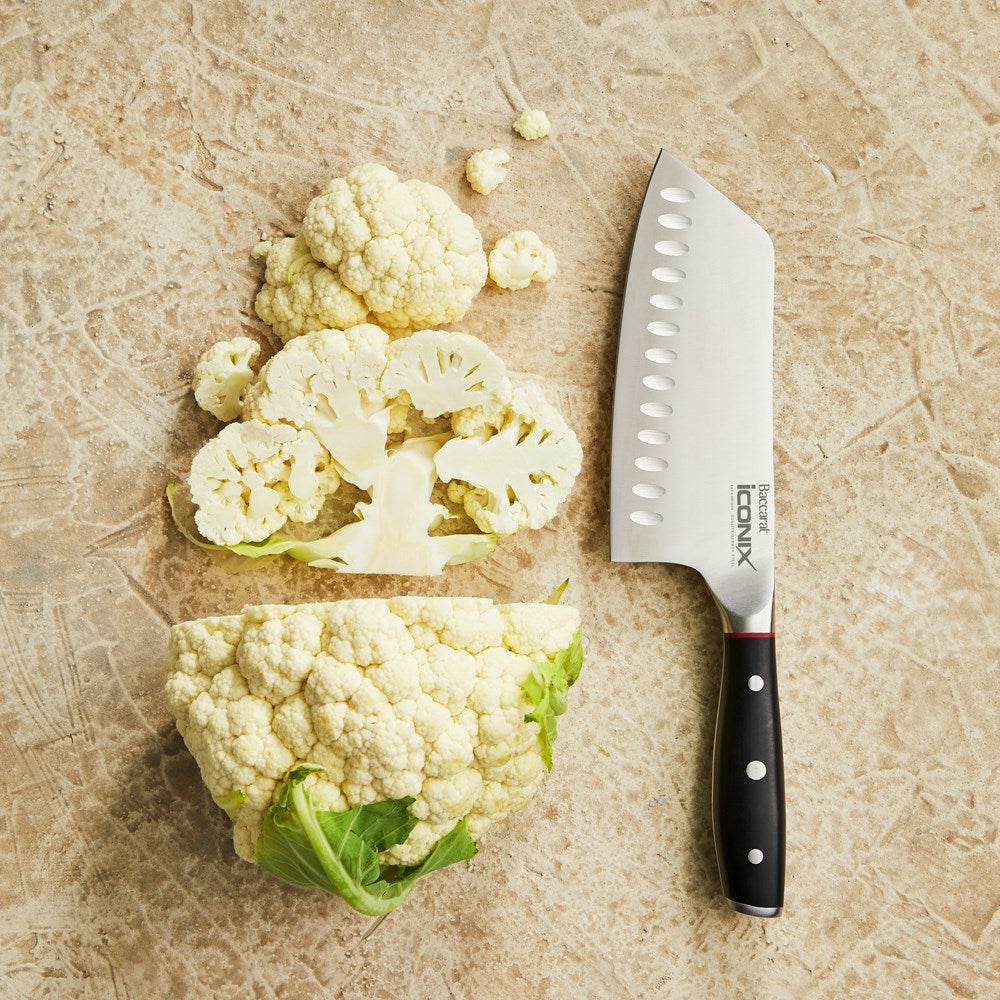 Chopped cauliflower on beige surface next to a silver cleaver knife with a black handle - Baccarat