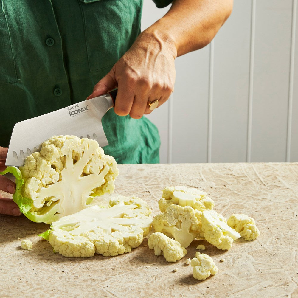 Chopped cauliflower on beige surface next to a silver cleaver knife with a black handle - Baccarat