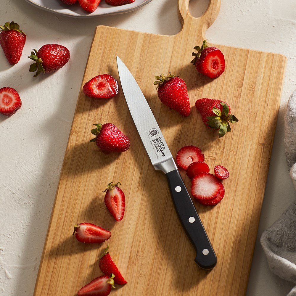 A black-handled knife on a wooden cutting board with sliced strawberries - Baccarat Wolfgang Starke