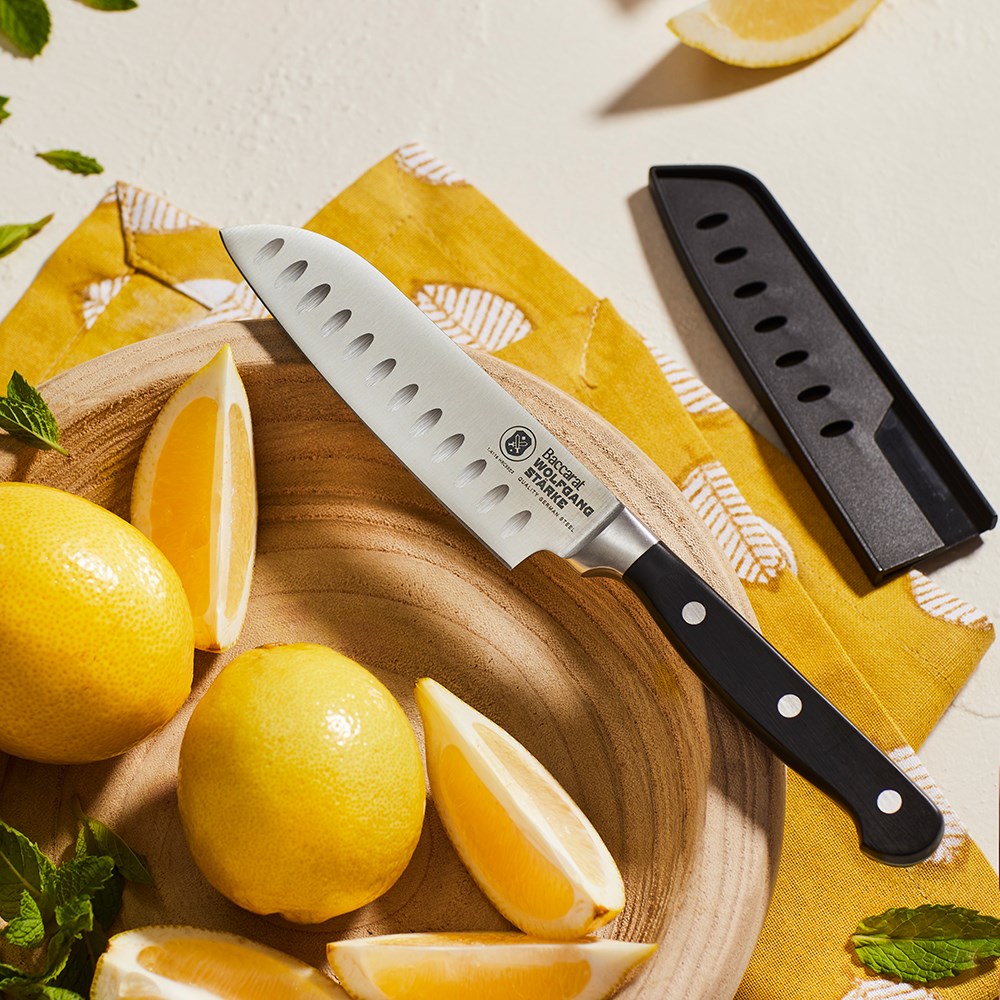Six santoku knives with silver blades and black handles on a gray surface - Baccarat Wolfgang Starke