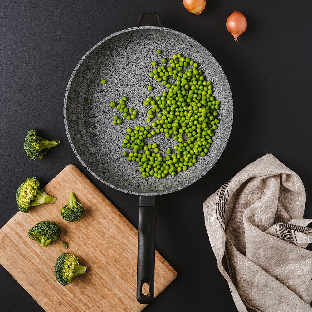 Frying pan with green peas on black surface wooden board with broccoli and onions nearby - Baccarat
