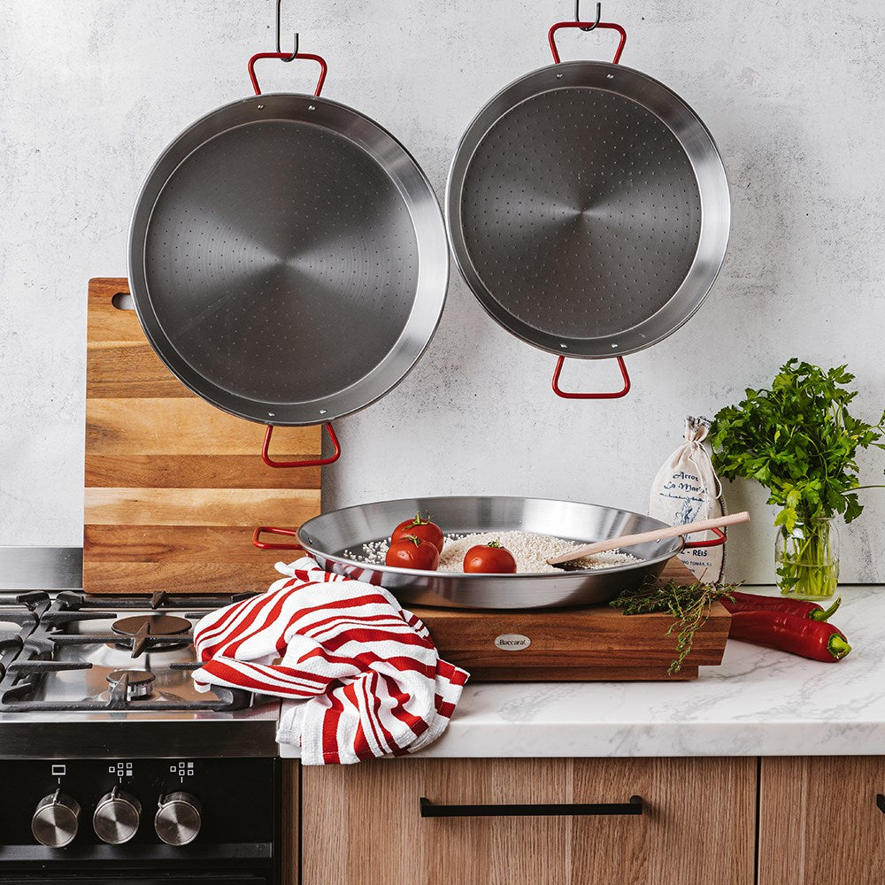 Two frying pans hanging on a white wall above a counter with a towel tomatoes and herbs - Baccarat