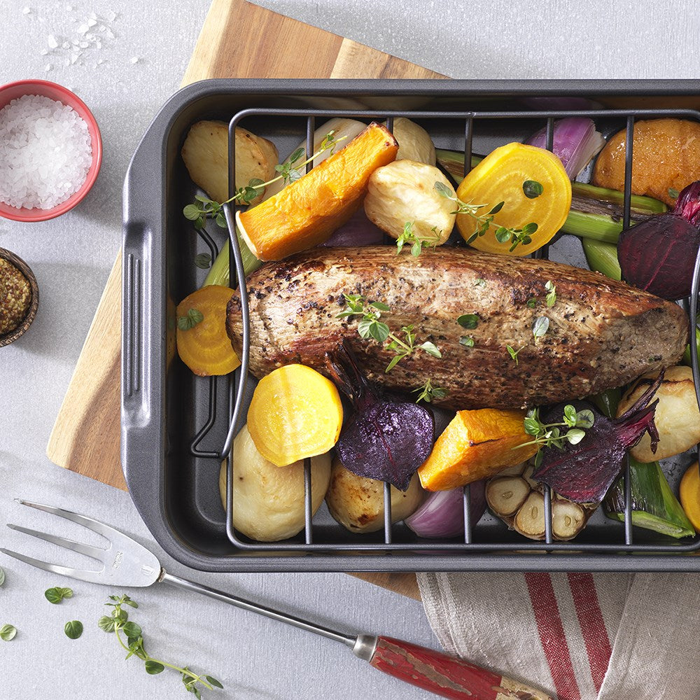 A baked dish in a grill on a wooden board garnished with herbs - Baccarat Carbon Steel Roast Grill