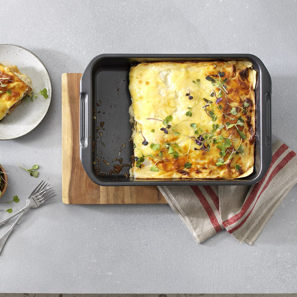 A baked dish in a grill on a wooden board garnished with herbs - Baccarat Carbon Steel Roast Grill