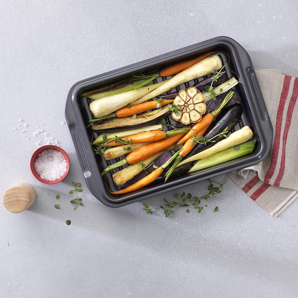 A baked dish in a grill on a wooden board garnished with herbs - Baccarat Carbon Steel Roast Grill