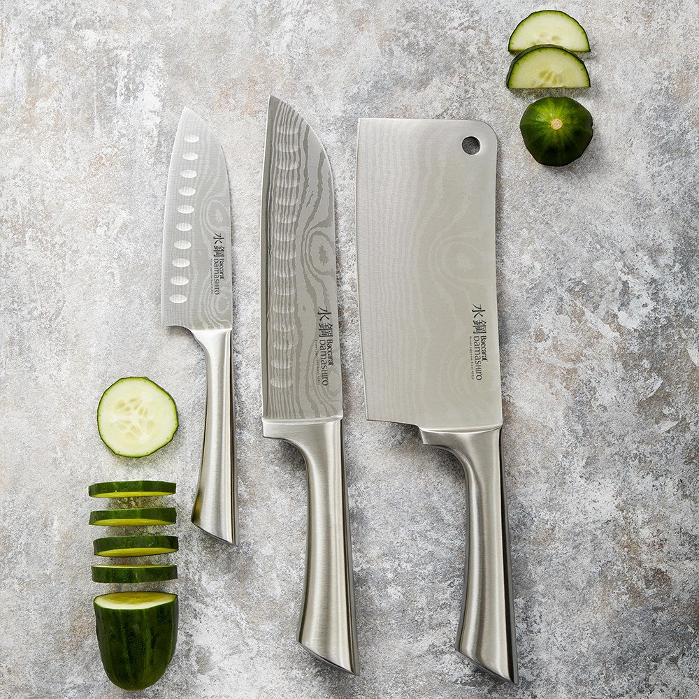 Three stainless steel knives next to whole and sliced limes grey surface - Baccarat Damashiro