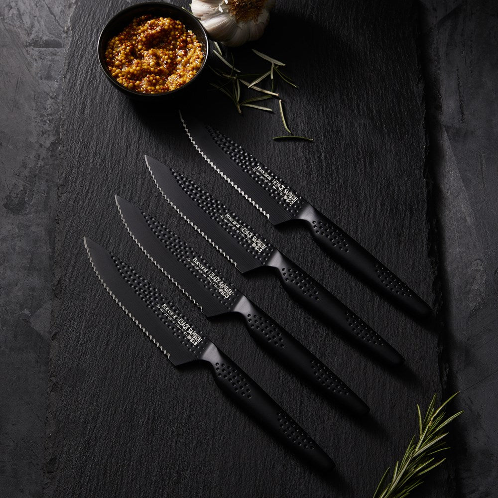 Elegant Baccarat Samurai Set of 4-piece steak knives lined up on dark slate with herbs and spices