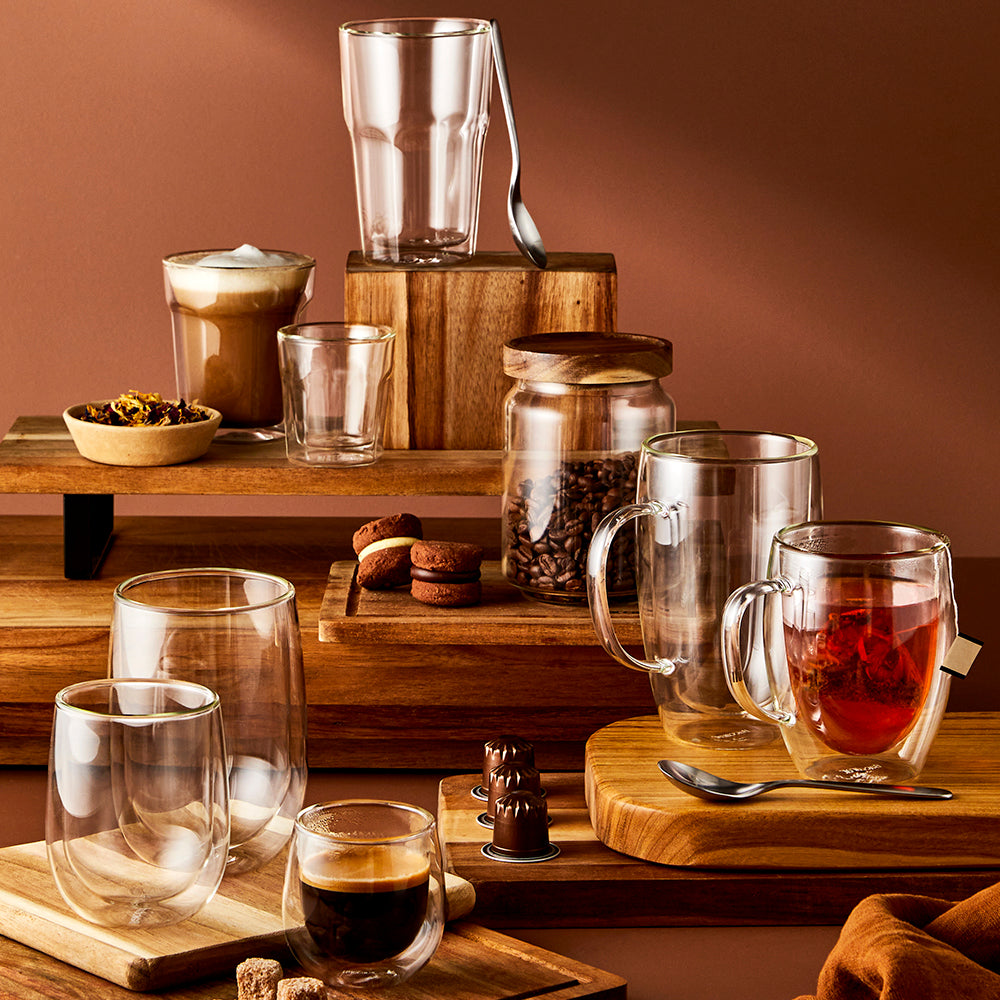 Two glass mugs of creamy iced coffee being poured against a dark background red casserole - Baccarat
