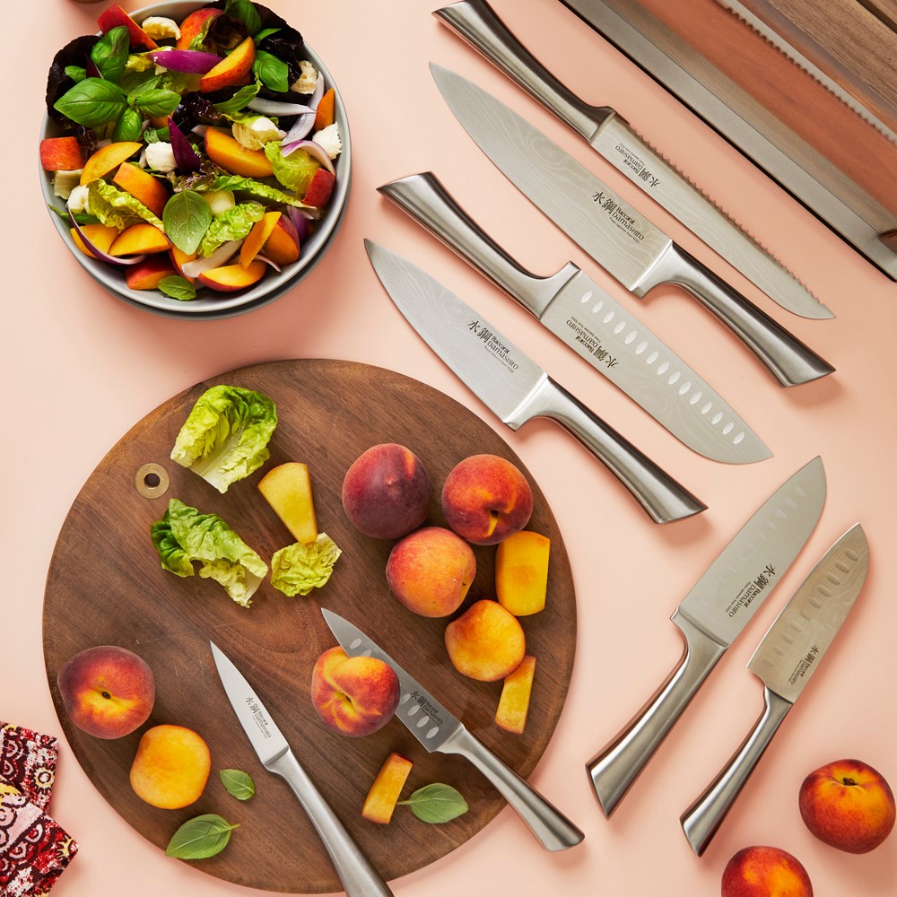 Slices of peaches on a wooden board next to a salad bowl and knives in the background - Baccarat