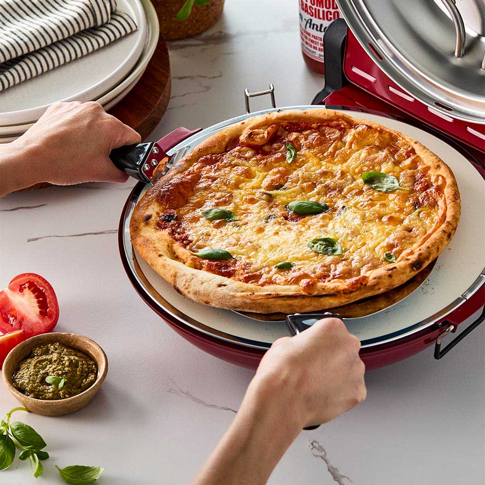 Red gourmet slice pizza oven with temperature dial beside a plant and tomato sauce bottle - Baccarat