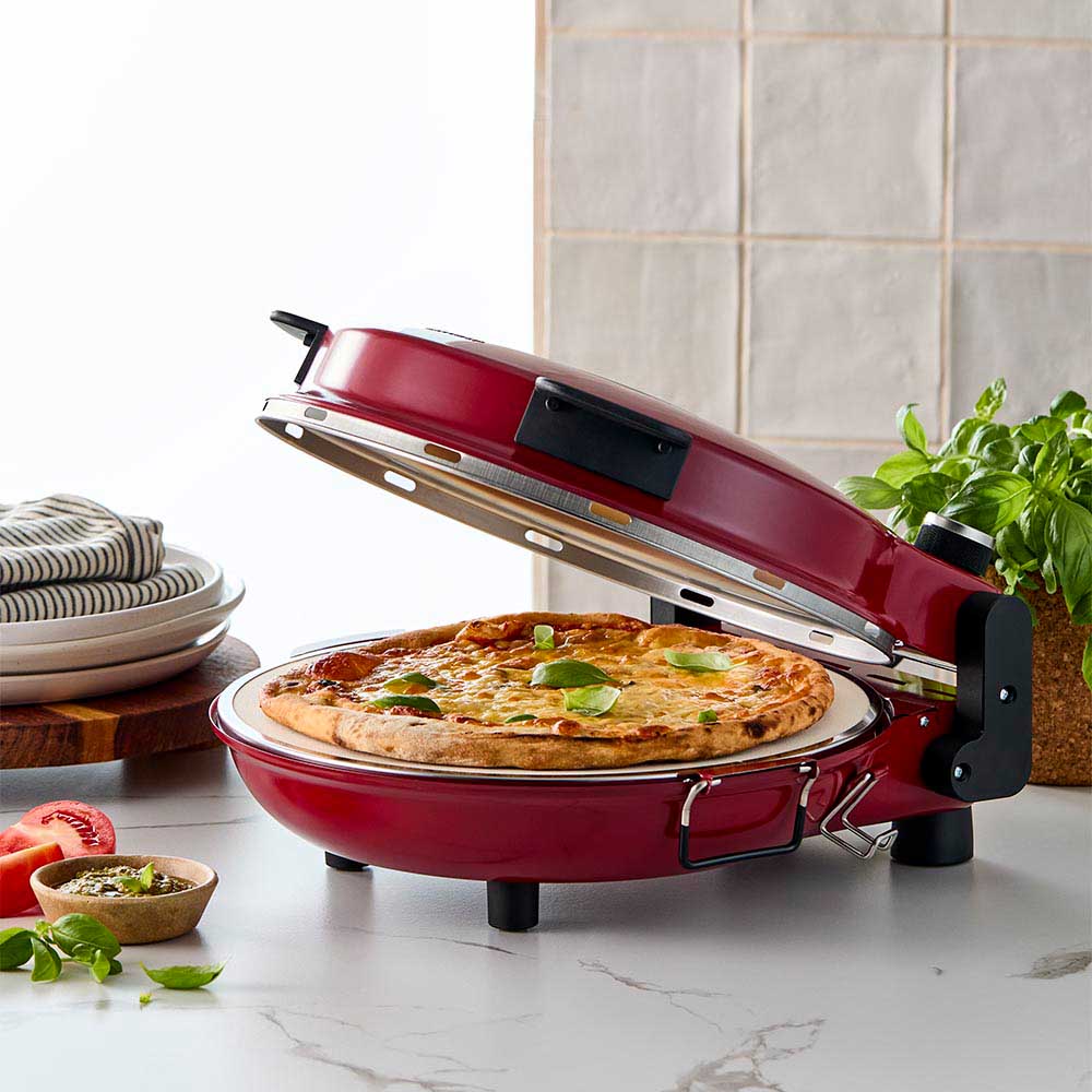 Red gourmet slice pizza oven with temperature dial beside a plant and tomato sauce bottle - Baccarat