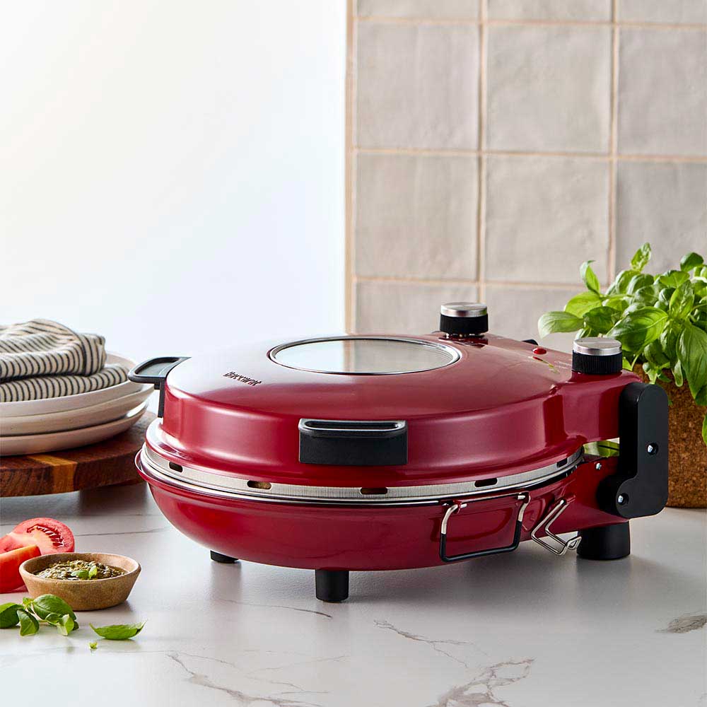 Red gourmet slice pizza oven with temperature dial beside a plant and tomato sauce bottle - Baccarat