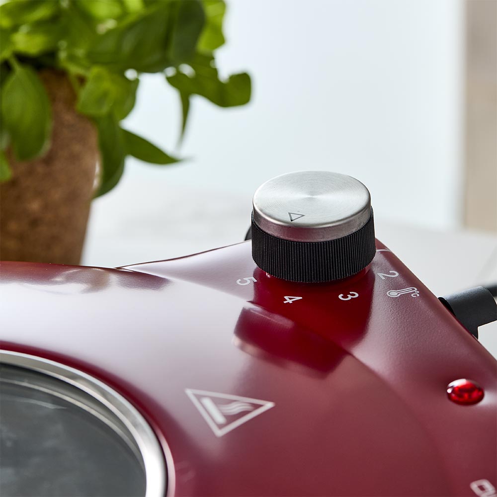 Red gourmet slice pizza oven with temperature dial beside a plant and tomato sauce bottle - Baccarat