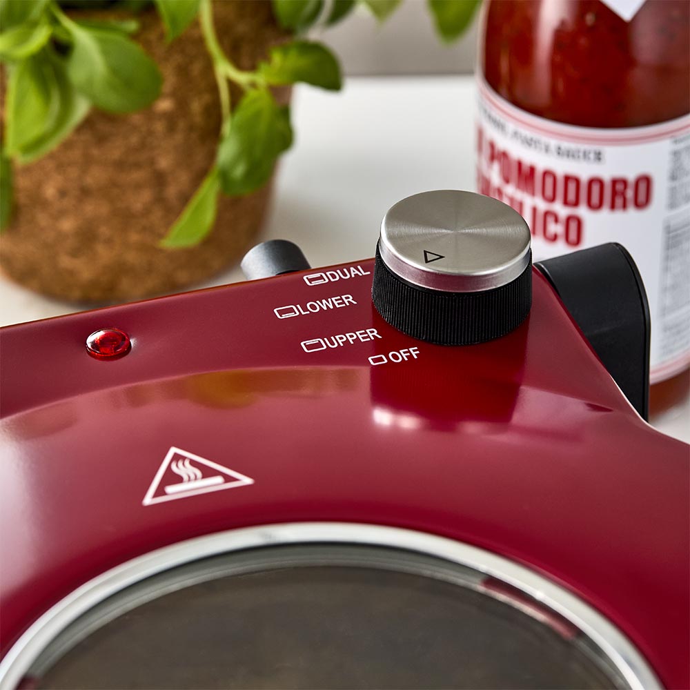 Red gourmet slice pizza oven with temperature dial beside a plant and tomato sauce bottle - Baccarat