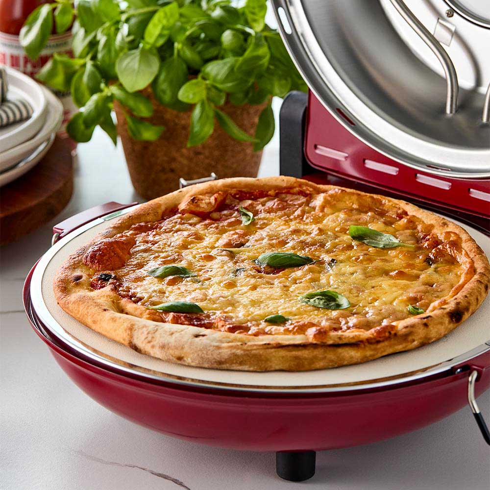 Red gourmet slice pizza oven with temperature dial beside a plant and tomato sauce bottle - Baccarat