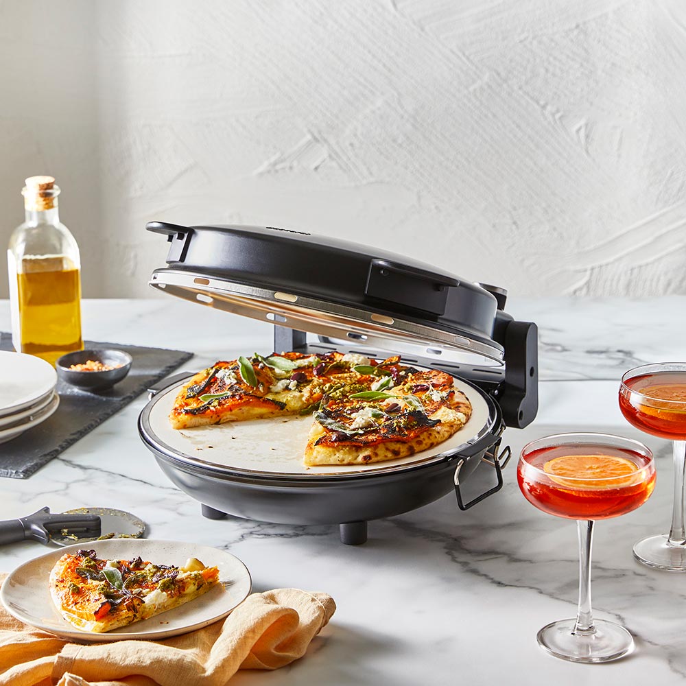 A pizza maker with a freshly cooked pizza red pizza oven surrounded by plates and drinks - Baccarat