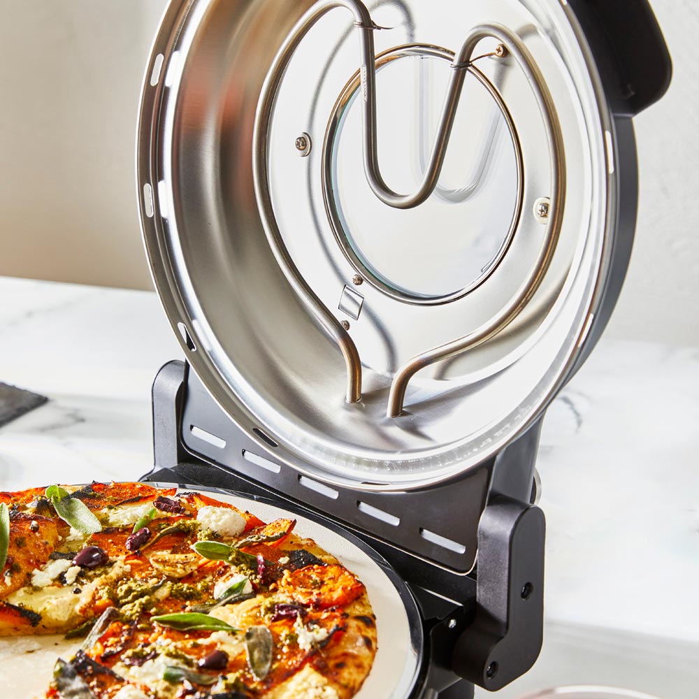 A pizza maker with a freshly cooked pizza red pizza oven surrounded by plates and drinks - Baccarat