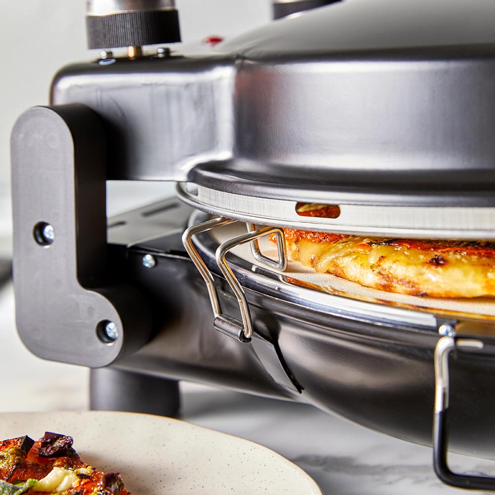 A pizza maker with a freshly cooked pizza red pizza oven surrounded by plates and drinks - Baccarat
