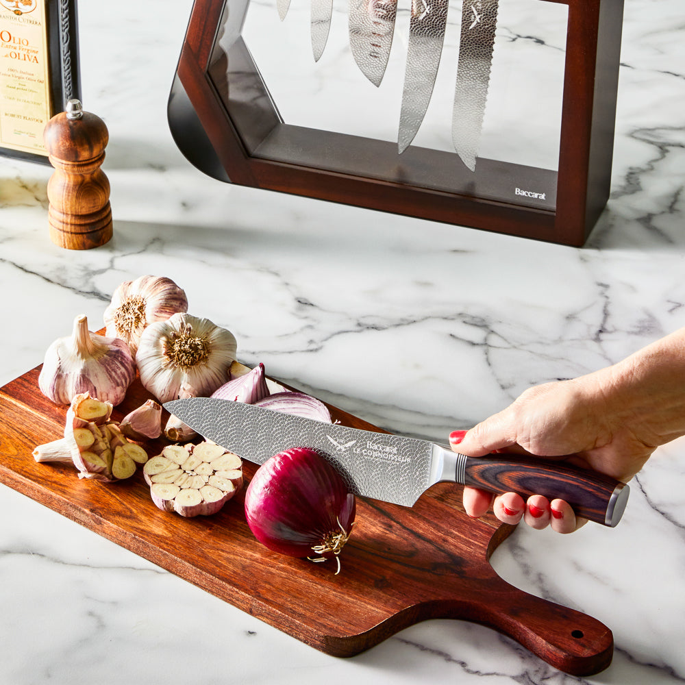 Chef's knife slicing garlic on a kitchen counter shiny silver blade 7 piece knife block - Baccarat