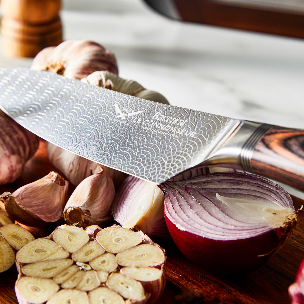 Chef's knife slicing garlic on a kitchen counter shiny silver blade 7 piece knife block - Baccarat