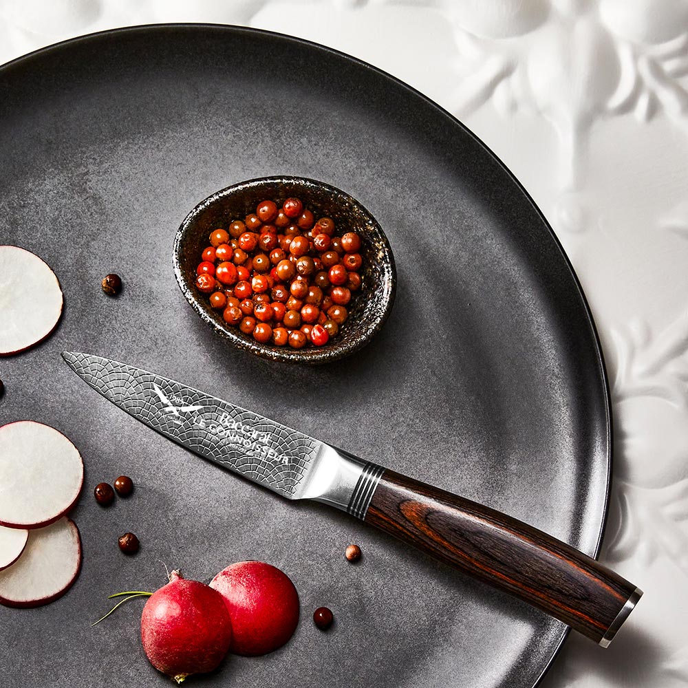 A collection of paring knives displayed on a white textured surface with brown handles - Baccarat