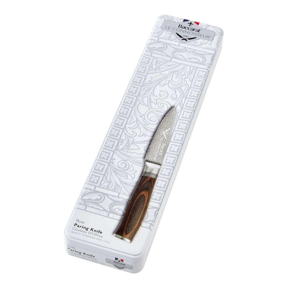 A collection of paring knives displayed on a white textured surface with brown handles - Baccarat
