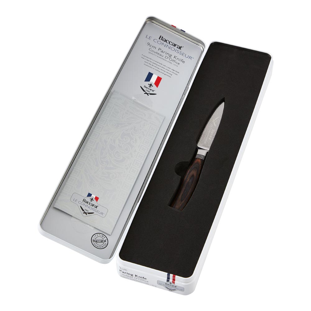 A collection of paring knives displayed on a white textured surface with brown handles - Baccarat
