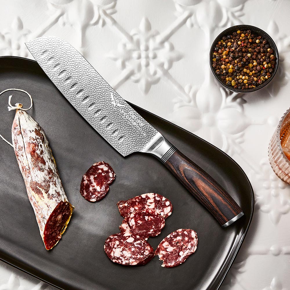Hands slicing cured sausage on a black slate board metal knife food - Santoku knife 14cm - Baccarat