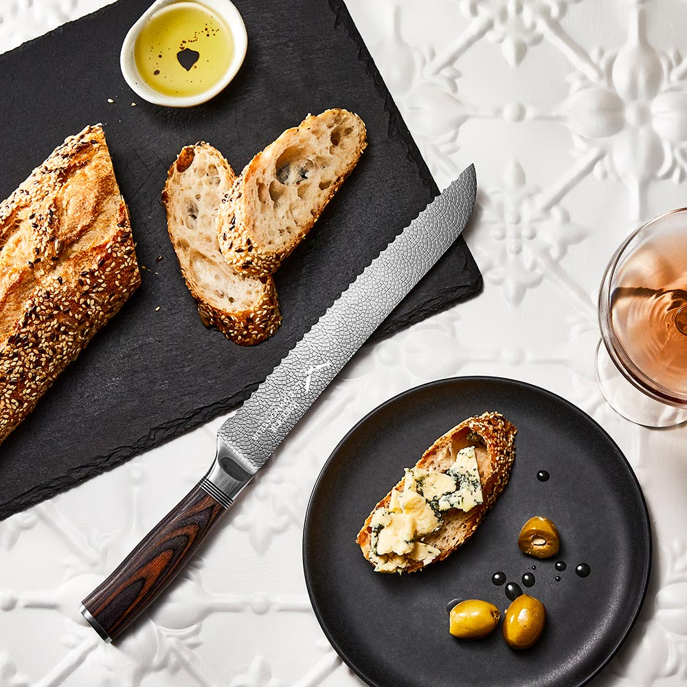 A rustic table setting with sliced bread and cheese featuring a silver bread knife 22cm - Baccarat
