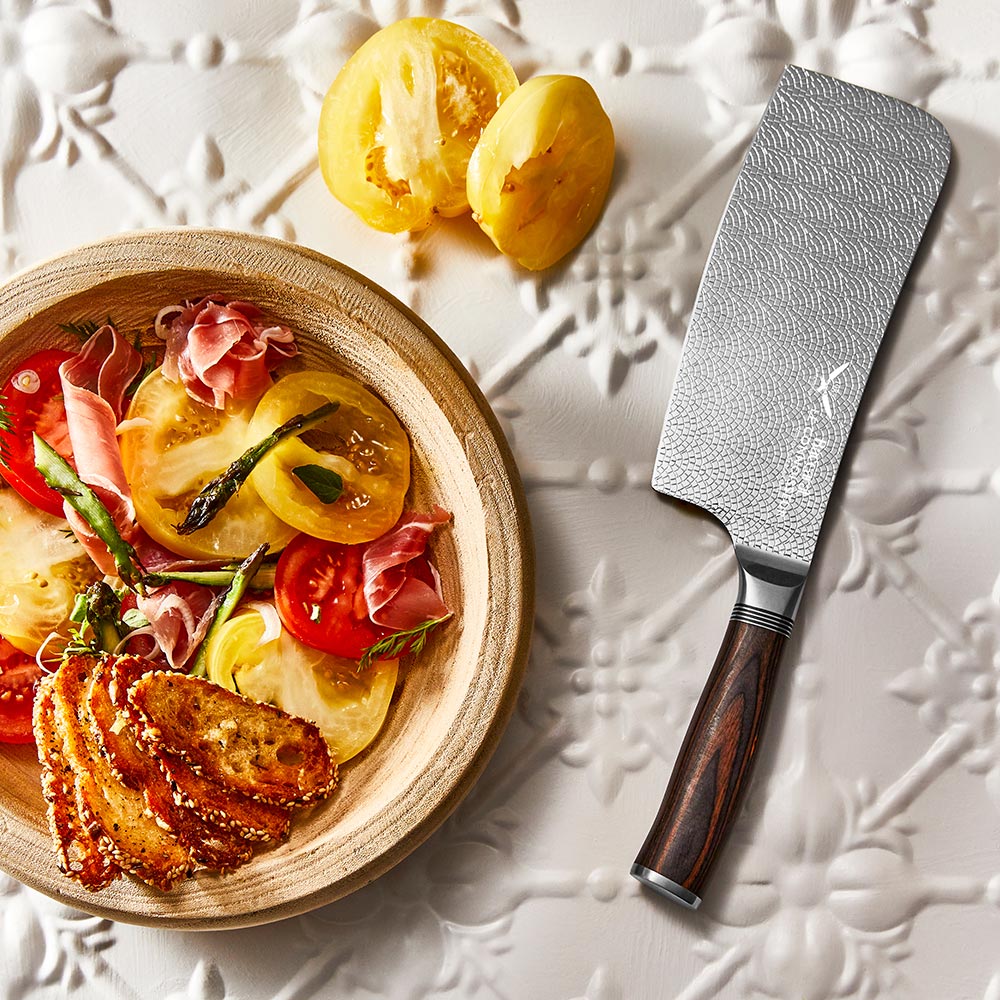 A hand slicing a red tomato with silver cleaver on a wooden cutting board - Baccarat Le Connoisseur