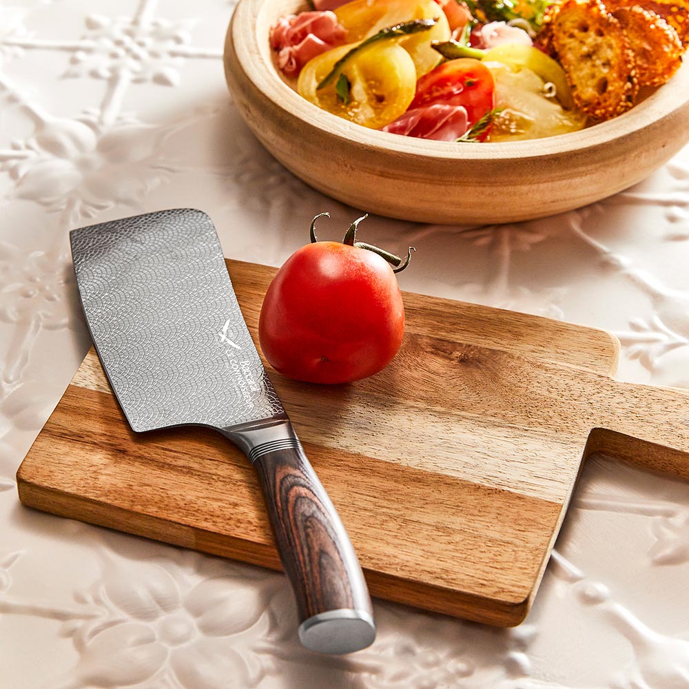 A hand slicing a red tomato with silver cleaver on a wooden cutting board - Baccarat Le Connoisseur