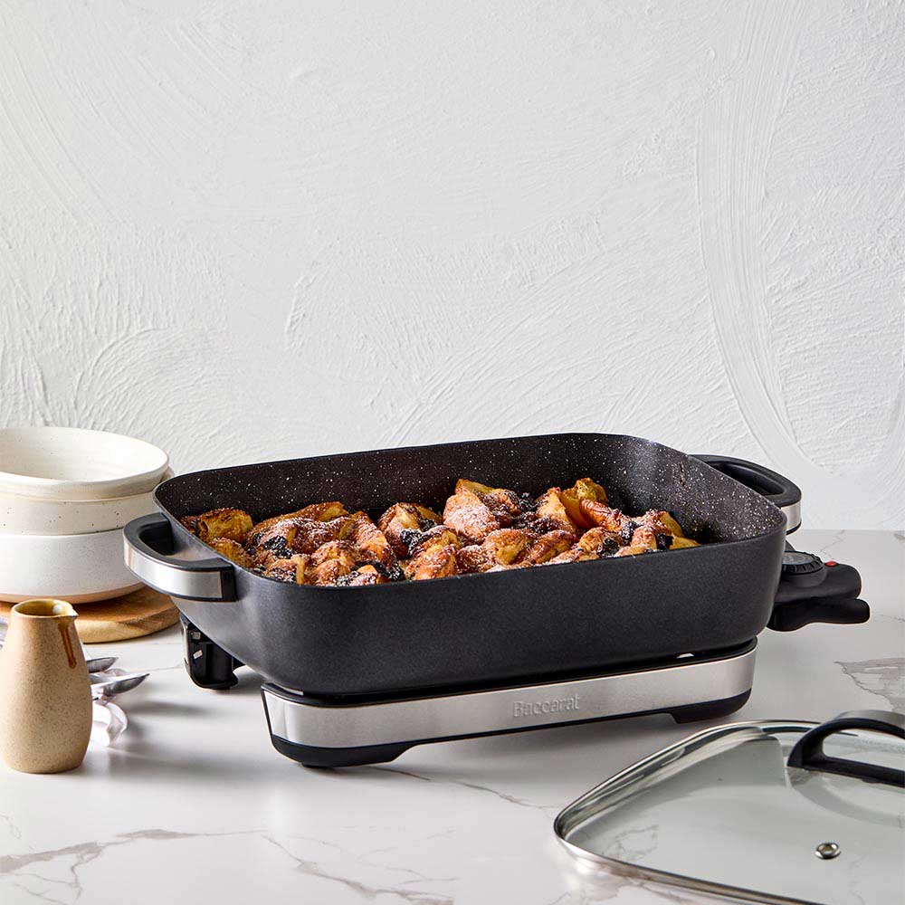 A black pan of bread pudding with a bowl of ice cream on a white countertop black frypan - Baccarat