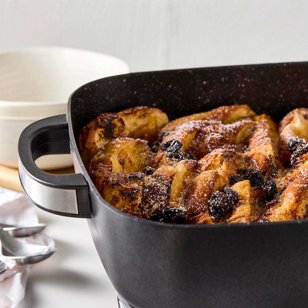A black pan of bread pudding with a bowl of ice cream on a white countertop black frypan - Baccarat