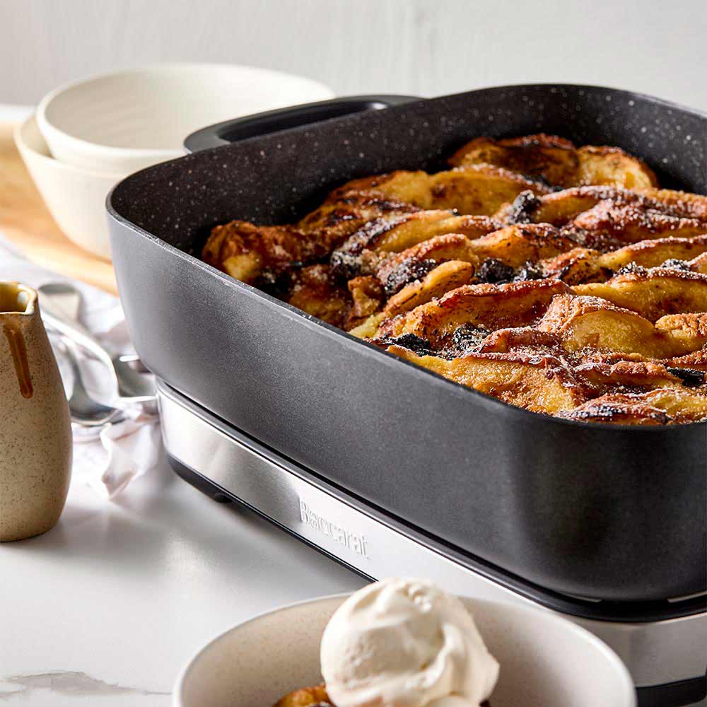 A black pan of bread pudding with a bowl of ice cream on a white countertop black frypan - Baccarat