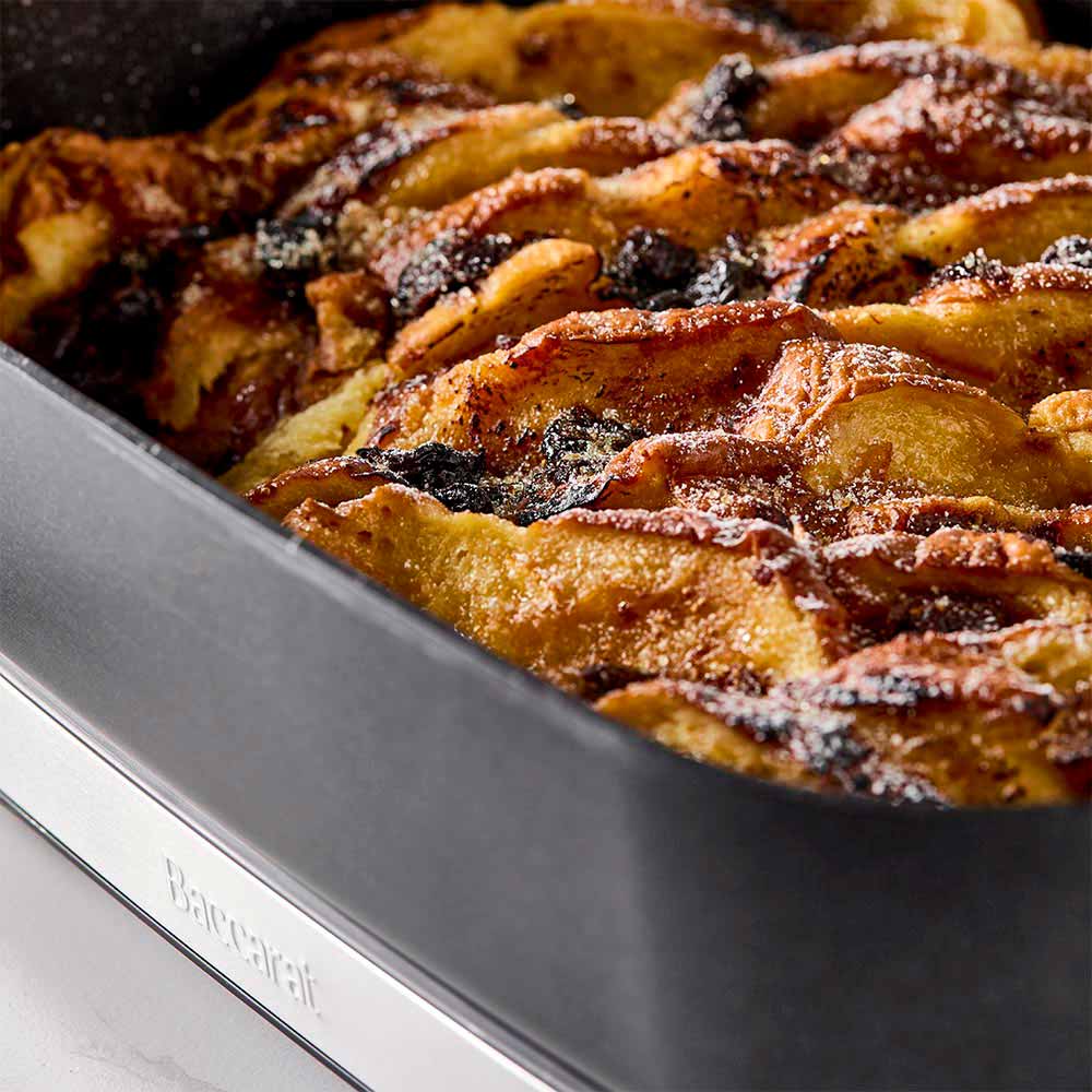 A black pan of bread pudding with a bowl of ice cream on a white countertop black frypan - Baccarat