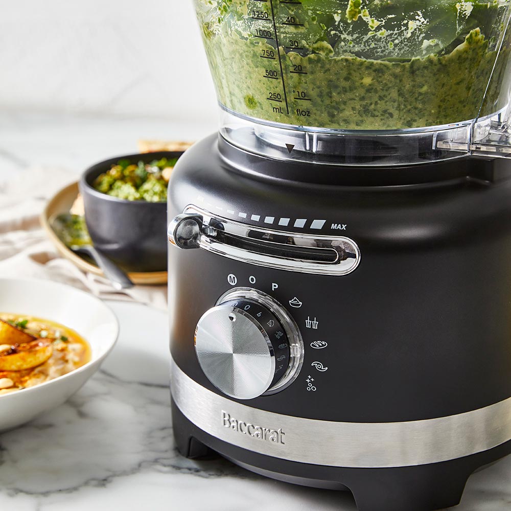 black air fryer with green ingredients on marble counter near dishes and a spice grinder - Baccarat