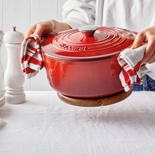 A hand gently holding a wooden trivet under a shiny red pot on a white surface red pot  - Baccarat