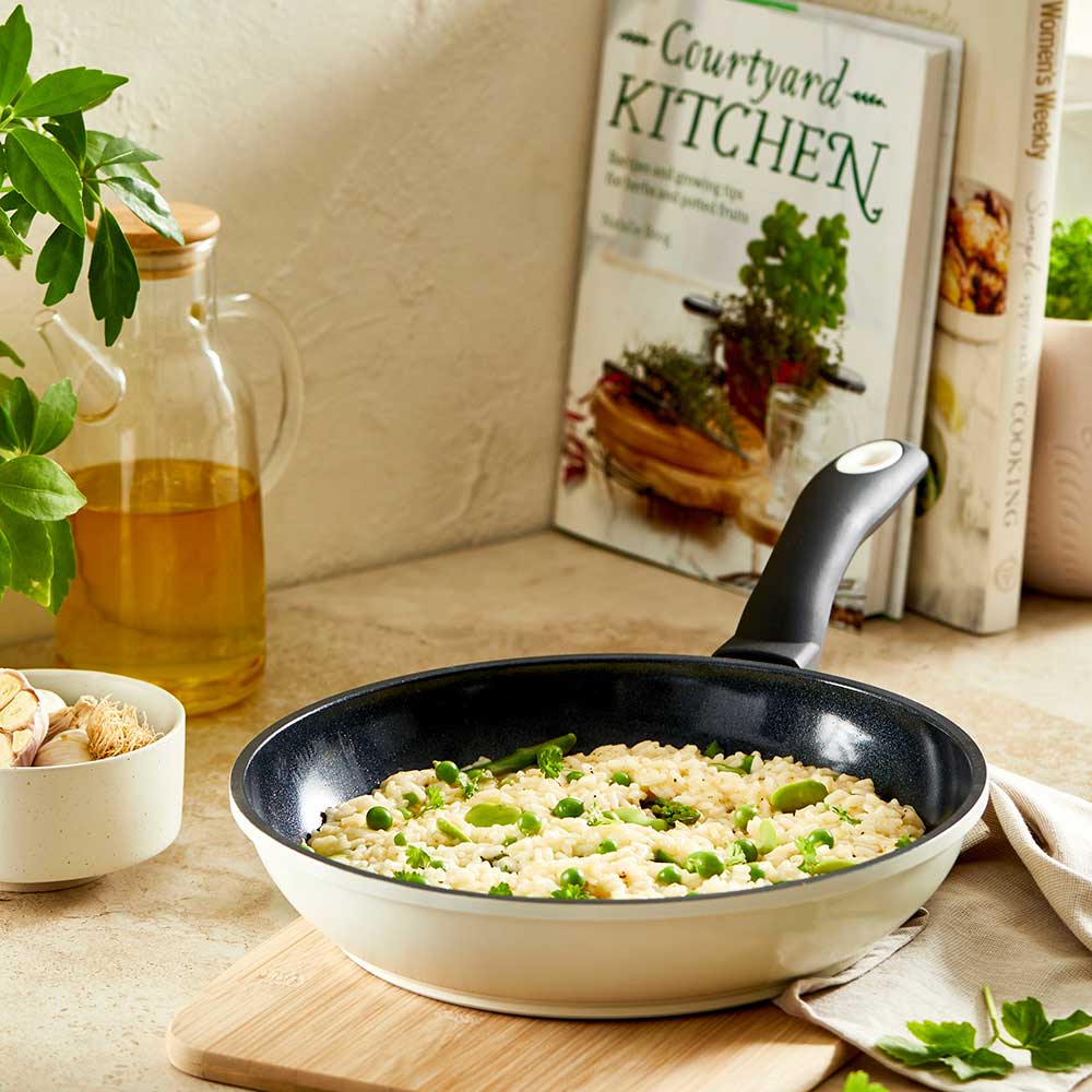 A creamy risotto with green peas in a white pan on a wooden board - cream bio frypan 20cm - Baccarat