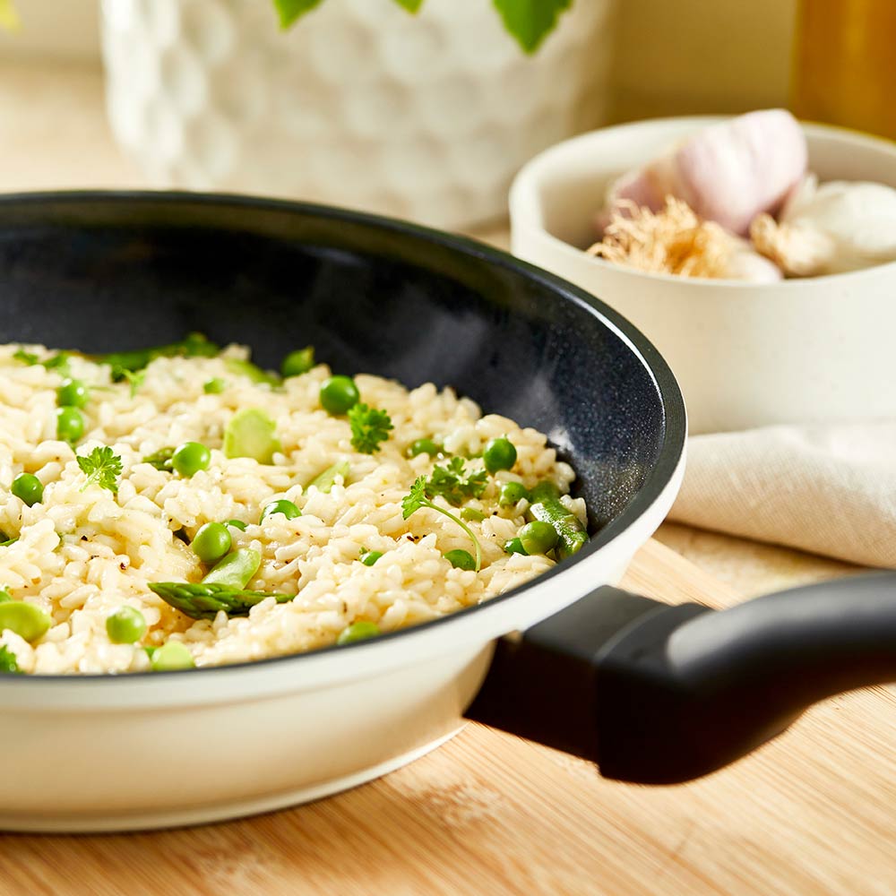 A creamy risotto with green peas in a white pan on a wooden board - cream bio frypan 20cm - Baccarat