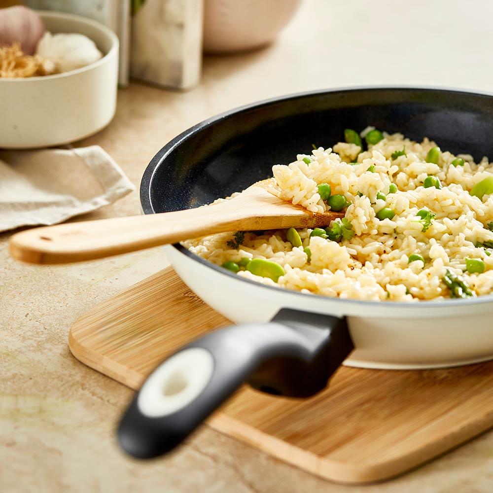 A creamy risotto with green peas in a white pan on a wooden board - cream bio frypan 20cm - Baccarat