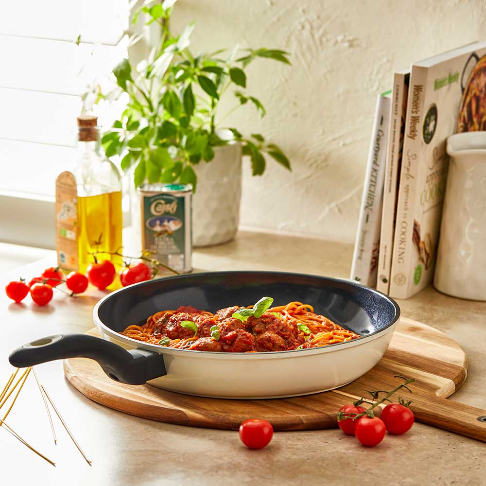 A 32-cm Baccarat Bio Frying pan containing pasta on a wooden board surrounded by fresh ingredients