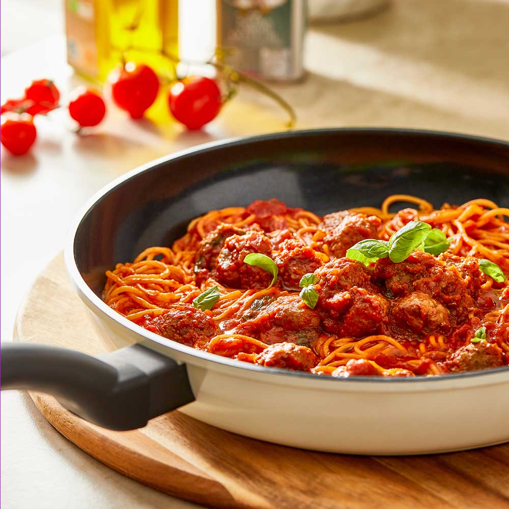 A 32-cm Baccarat Bio Frying pan containing pasta on a wooden board surrounded by fresh ingredients