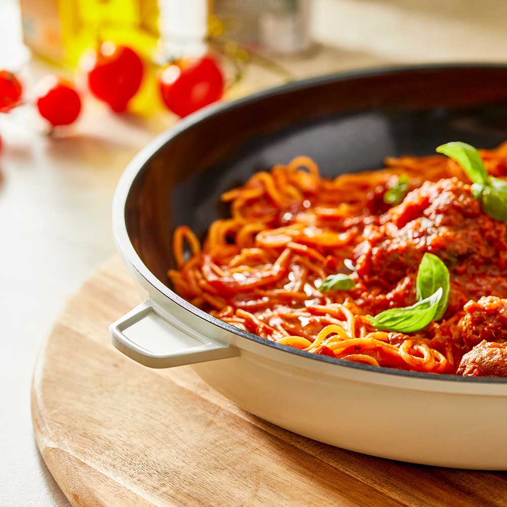 A 32-cm Baccarat Bio Frying pan containing pasta on a wooden board surrounded by fresh ingredients