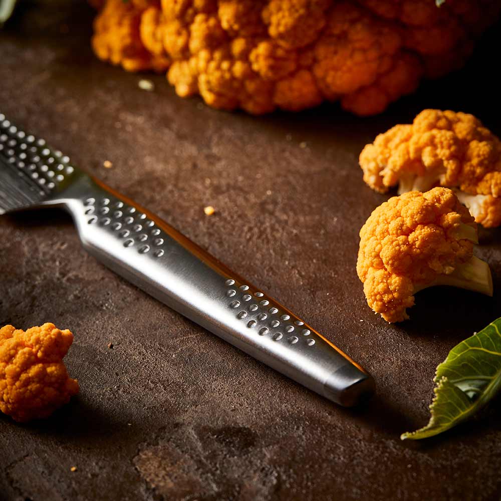 Close-up of a silver utility knife on a wooden surface and orange cauliflower - Baccarat id3 Samurai