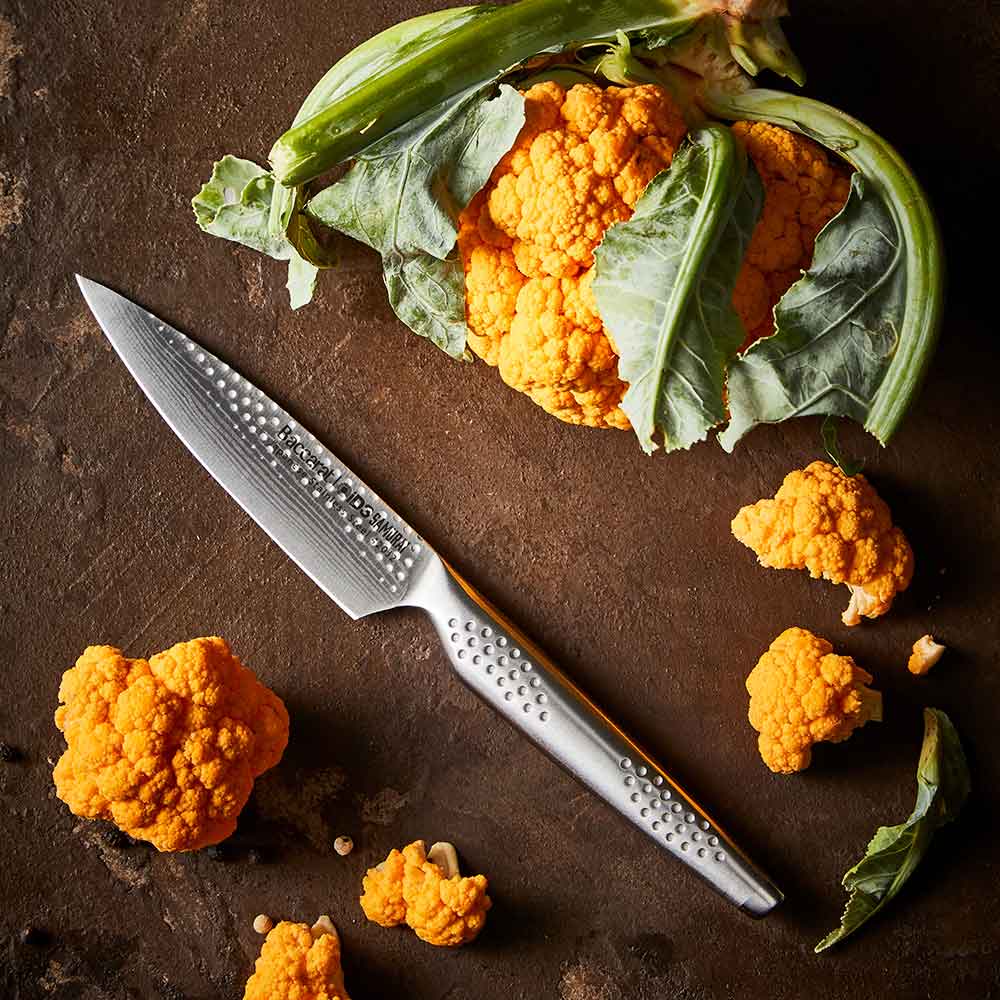 Close-up of a silver utility knife on a wooden surface and orange cauliflower - Baccarat id3 Samurai