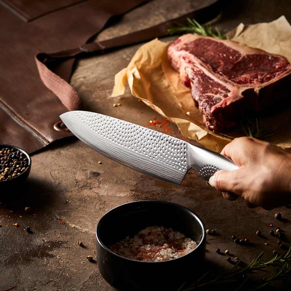 A person chops herbs in a kitchen with large steak in background on a wooden board - Baccarat