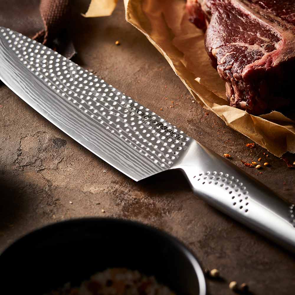 A person chops herbs in a kitchen with large steak in background on a wooden board - Baccarat